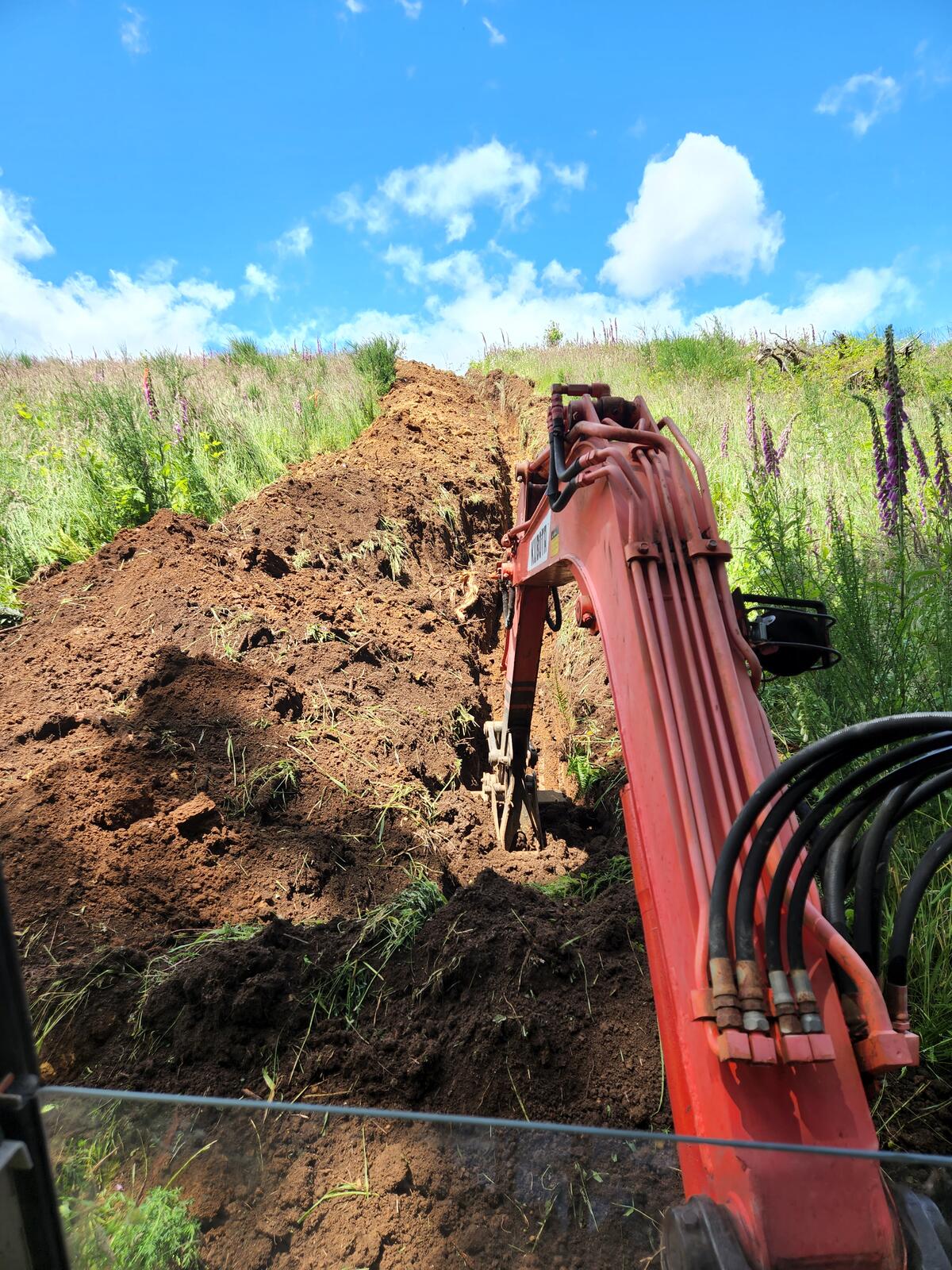 Kubota excavator digging the utility trench across the upper meadow